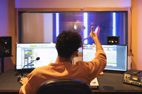 Faceless male audio engineer with mixing board and computer showing thumb up to anonymous singer while recording song in musical studio - ADSF47507