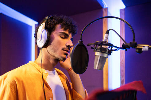 Side view of male professional singer in headphones and microphone creating music in studio - ADSF47509