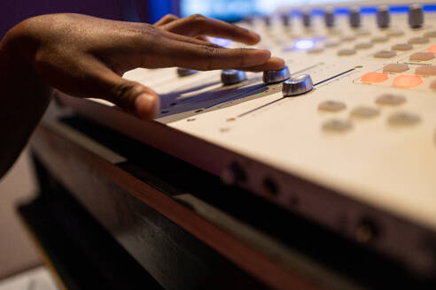 Crop anonymous African American female audio engineer creating music and using mixing board and sound software in control room - ADSF47513