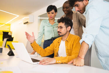 Group of multiracial coworkers gathering together at table and working on project using laptop in modern office - ADSF47546