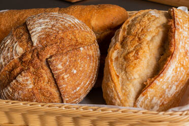 Focused of various tasty freshly baked pastry breads being served with baking pan into wicker basket with fabric on dining table indoors - ADSF47568