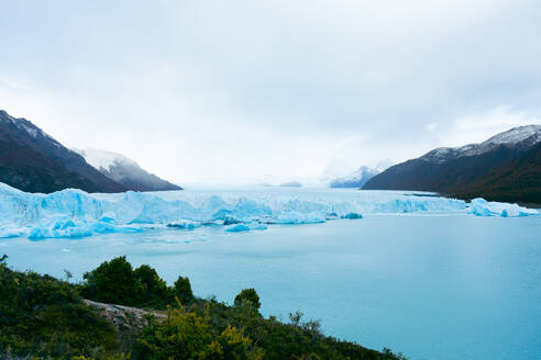 Picturesque view of blue frozen river with snowy glacier mountains against white sky background in winter at Perito Moreno Argentina - ADSF47598