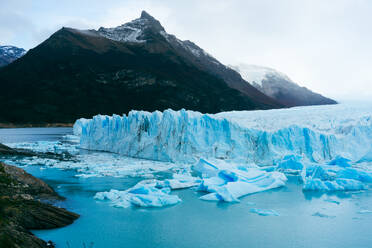 Picturesque view of blue frozen river with snowy glacier mountains against white sky background in winter at Perito Moreno Argentina - ADSF47600