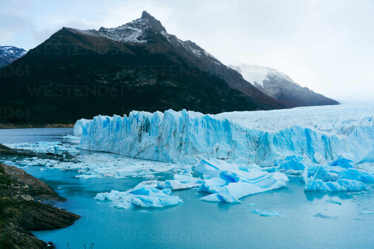 Picturesque view of blue frozen river with snowy glacier mountains against  white sky background in winter at Perito Moreno Argentina stock photo