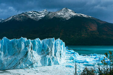 Scenic view of rough mountain range with glacier peaks and seabed covered with white ice and snow against dark blue cloudy sky in winter at Perito Moreno Argentina - ADSF47602
