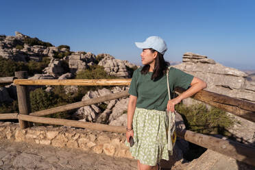 Back view of slim young woman standing on stone barrier near sea and  looking away on sunny day in Nerja, Spain stock photo