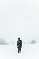 Male in warm outerwear standing in snowdrift in snowy valley against bare trees during blizzard in cold winter day in Madrid - ADSF47657