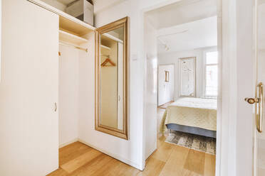 Narrow corridor with white walls and doors leading to spacious room with windows and parquet floor in modern apartment - ADSF47681