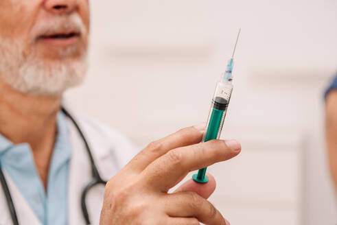 Crop anonymous male doctor in medical uniform with syringe filled by vaccine in hand working in hospital - ADSF47719