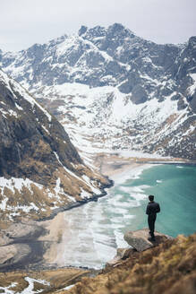 From above of back view of unrecognizable tourist standing on rocky edge admiring magnificent mountains and sea in Lapland - ADSF47740