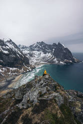 From above of side view of anonymous tourist sitting on rocky edge admiring magnificent mountains and sea in Lapland - ADSF47743