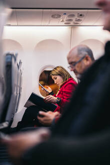 Side view of passengers sitting on seats near window with magazine and smartphones in aircraft while waiting for flight in airport in Lapland - ADSF47745