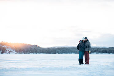 Happy boyfriend enjoying hugging girlfriend on romantic date on winter weekend against snowy trees in woods in sunset in Lapland - ADSF47746