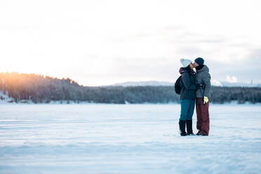Side view of boyfriend enjoying kissing and hugging girlfriend on romantic date on winter weekend against snowy trees in woods in sunset in Lapland - ADSF47747