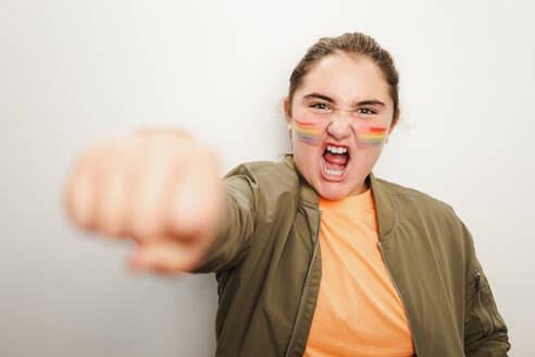 Excited fun loving teenage girl with opened mouth looking at camera while standing in karate pose with blurred closed fist against gray wall in light - ADSF47757