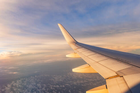 Breathtaking view of white wing of aircraft flying in blue sky over colorful fluffy cumulus clouds in sunset - ADSF47762