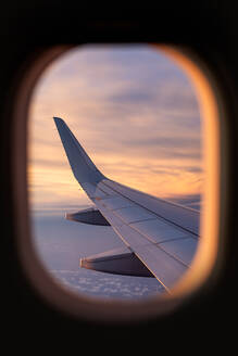 Majestic view through window of wing of plane in colorful cloudscape while jet flying high against sky in sunset - ADSF47763