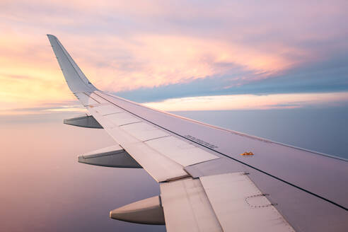 Breathtaking view of white wing of aircraft flying in blue sky over colorful fluffy cumulus clouds in sunset - ADSF47764