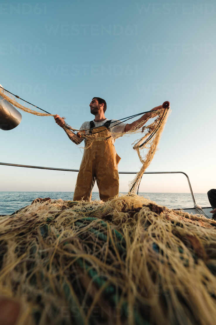 From below focused bearded male fisher in uniform seiner hunting fish with  net while working on