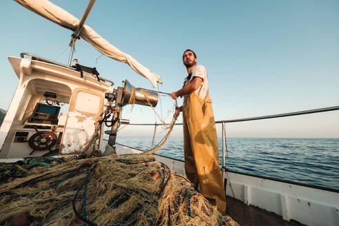 Von unten fokussiert bärtigen männlichen Fischer in Uniform seiner Jagd nach Fischen mit dem Netz bei der Arbeit auf Schoner in Soller in der Nähe von Baleareninsel von Mallorca - ADSF47836