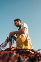 Weichzeichner eines bärtigen männlichen Fischers in einer Schürze, der sein Netz bei der Fischjagd auf einem Trawler in Soller in der Nähe der Baleareninsel Mallorca losbindet - ADSF47839