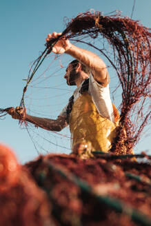 Weichzeichner eines bärtigen männlichen Fischers in einer Schürze, der sein Netz bei der Fischjagd auf einem Trawler in Soller in der Nähe der Baleareninsel Mallorca losbindet - ADSF47840