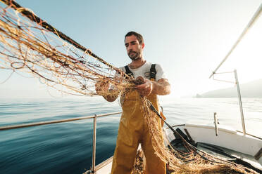 Von unten fokussiert bärtigen männlichen Fischer in Uniform seiner Jagd nach Fischen mit dem Netz bei der Arbeit auf Schoner in Soller in der Nähe von Baleareninsel von Mallorca - ADSF47842