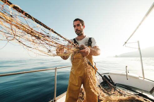 Von unten fokussiert bärtigen männlichen Fischer in Uniform seiner Jagd nach Fischen mit dem Netz bei der Arbeit auf Schoner in Soller in der Nähe von Baleareninsel von Mallorca - ADSF47842