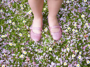 Junges Mädchen Füße und Beine tragen rosa Schuhe stehen auf einem Rasen mit Blütenblättern und Blumen bedeckt - FSIF06556