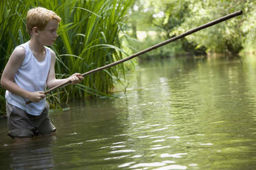 Young boy fishing in a river with his legs in the water - FSIF06562