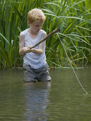 Young boy fishing in a river with his legs in the water - FSIF06563