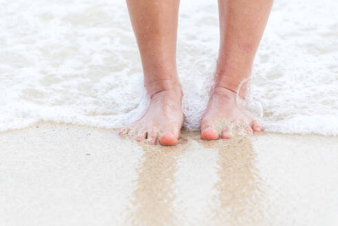 Woman bare foot walking on the summer beach. close up leg of young woman walking along wave of sea water and sand on the beach. Enjoyment barefoot walk outdoor with freedom. Relaxation Travel Concept. - INGF12125