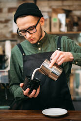 Waiter in black hat fill in a cup of milk, blur background. - INGF12129