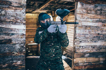 Male paintball player with marker gun in hands, front view, focus on weapon, winter battle. Extreme sport game, soldier fights in protection mask and uniform. Paintball player with marker gun, front view - INGF12132