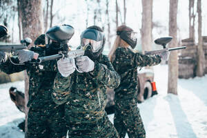 Paintball players in uniform and masks poses with marker guns in hands after winter forest battle. Extreme sport game. Paintball players in uniform and masks poses - INGF12134