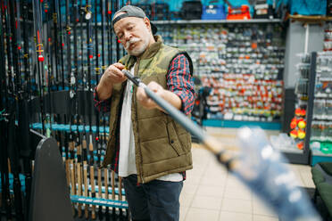 Male angler choosing rod in fishing shop. Equipment and tools for fish catching and hunting, accessory choice on showcase in store, spinnings and telescopes assortment. Male angler choosing rod in fishing shop - INGF12140