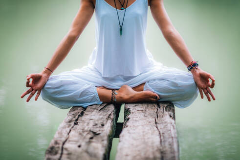 Beautiful young woman doing yoga exercise by the lake. Sitting in lotus position - INGF12146