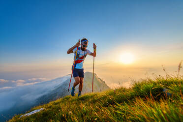 Mann mit Stöcken in den Bergen mit Sonnenuntergang im Hintergrund - INGF12151