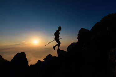Sunset silhouette of skyrunner man climbing alpine ridge with poles - INGF12152