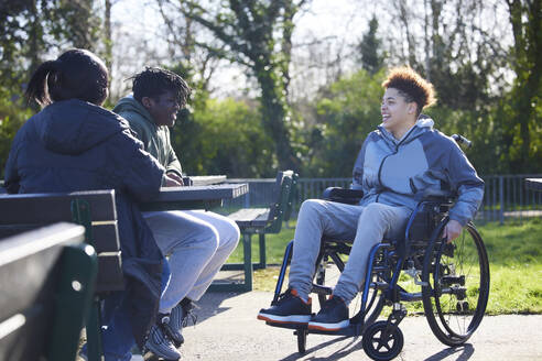 Teenage Girl In Wheelchair Hanging Out Talking And Laughing With Friends In Park - INGF12160