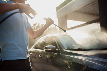 Mann hält Hochdruck-Wasserpistole, Hand-Autowaschanlage. Autowaschanlagen-Industrie oder -Geschäft. Männliche Person reinigt sein Fahrzeug von Schmutz im Freien. Mann hält Hochdruck-Wasserpistole, Hand-Autowäsche - INGF12169