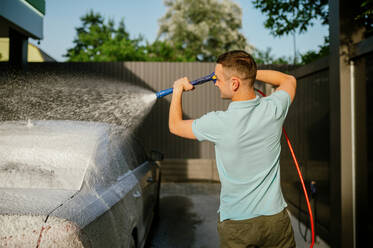 Mann mit Hochdruck-Wasserpistole mit Schaum, Hand-Autowaschanlage. Autowaschanlagen-Industrie oder -Geschäft. Männliche Person reinigt sein Fahrzeug von Schmutz im Freien. Mann mit Wasserpistole mit Schaum, Hand-Autowäsche - INGF12170