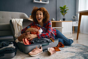 Funny woman having fun pack stuff clothes. Excited young girl laughing preparing for vacation trip. Funny woman packing luggage for vacation trip - INGF12174