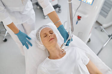 Top view woman client lying on medicinal couch getting skin treatment at professional beauty clinic. Woman client getting skin treatment at professional beauty clinic - INGF12193