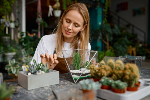 A woman making composition in florarium vase. Happy florist creating succulent plants composition. A woman making composition in florarium vase - INGF12198