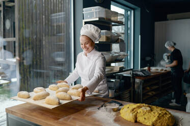 Woman baker engaged in making of traditional yeast buns with cheese. A woman baker making of traditional yeast buns with cheese - INGF12204