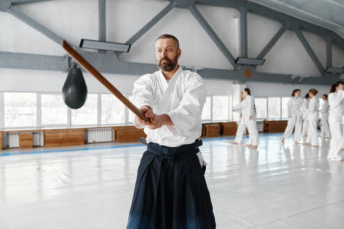 Portrait of aikido sensei master with wooden sword at group training. Learning fight with bamboo boken. Portrait of aikido sensei master with wooden sword at group training - INGF12213