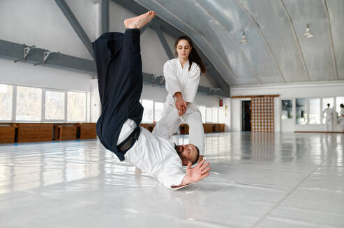 Talented female student throwing aikido teacher on floor during sparring and self defense training in gym. Talented female student throwing aikido teacher on floor - INGF12214