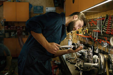 Male mechanic character working in garage on weekend. Man technician engaged on inspection of repaired wheel shaft spare part for motorcycle. Male mechanic character working in garage repairing motorcycle - INGF12215