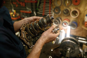 Motorcycle repair service indoor with closeup view on serviceman working with gear shaft. Cropped shot of mechanic hands holding spare part of motorbike for inspection. Motorcycle repair service indoor with closeup on serviceman hands holding gear - INGF12216